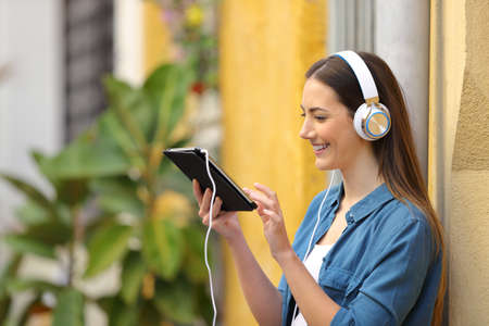 Happy girl listening and watching tablet online content in the streetの写真素材