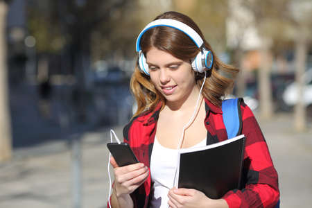 Student listens to music with headphones and smart phone walking in the streetの写真素材