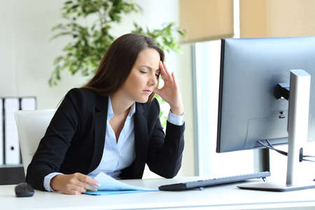Worried office worker suffering headache and complaining at workplaceの写真素材