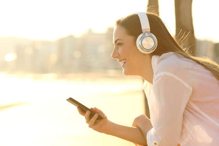 Side view portrait of a happy girl listening to music contemplating the beach at sunsetの写真素材
