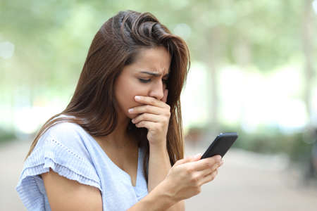 Sad girl complaining reading bad news on smart phone in the street