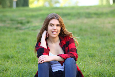 Happy teenage girl looks at camera sitting on the grass in a park