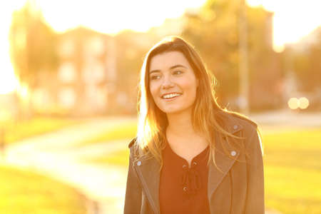 Front view portrait of a happy teen distracted walking in the street at sunset