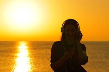 Front view of a woman silhouette listening to music at sunset on the beachの写真素材