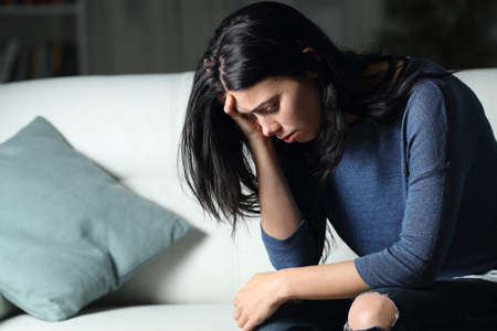 Sad woman complaining alone sitting on a couch in the dark night at homeの写真素材