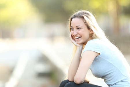 Happy teenage girl laughing looking away sitting in a park with copy spaceの写真素材