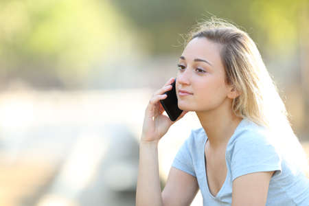 Serious teenage girl talking on smart phone sitting in a parkの写真素材