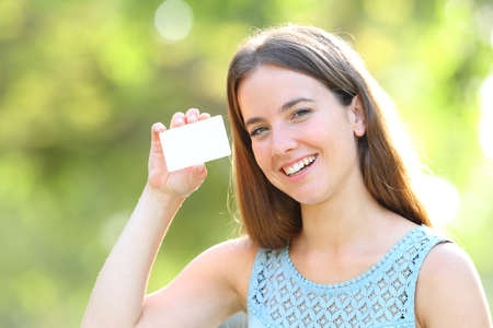 Happy woman showing a blank credit card looking at camera standing in a parkの写真素材