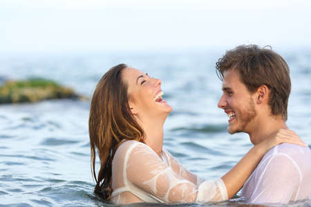 Side view portrait of a happy spontaneous couple joking in the water on the beachの写真素材