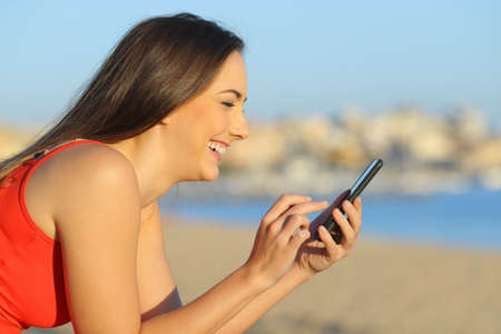 Happy teen searching content on smart phone on the beach a sunny dayの写真素材