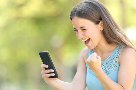 Girl finding exciting online content on smart phone in a park with a green backgroundの写真素材