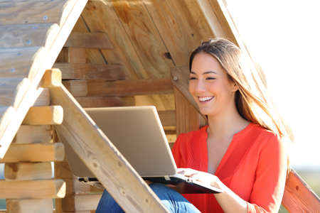 Happy woman using a laptop sitting in a wooden toy houseの写真素材