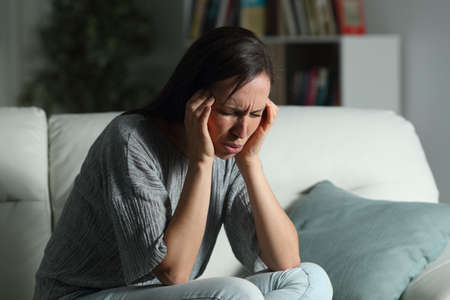 Woman suffering migraine in the night sitting on a couch in the living room at homeの写真素材