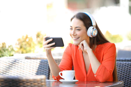 Happy woman watching media on smart phone sitting in a restaurant terraceの写真素材