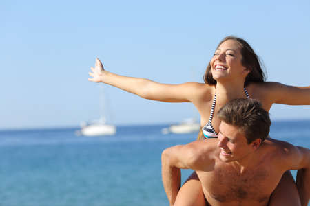 Happy couple joking piggibacking celebrating summer vacation on the beachの写真素材