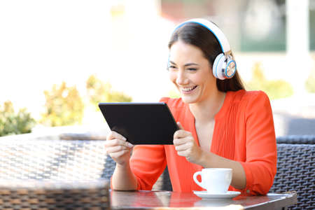 Happy female watching media content on tablet sitting in a coffee shop terraceの写真素材