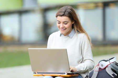 Happy student e learning using a laptop sitting in the streetの写真素材