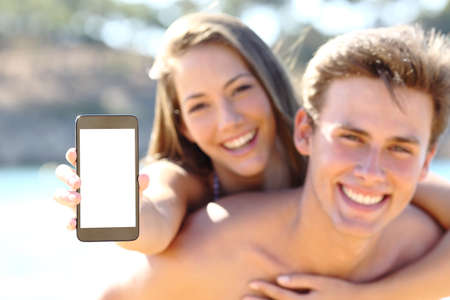 Happy couple on the beach showing blank phone screen on summer vacationの写真素材