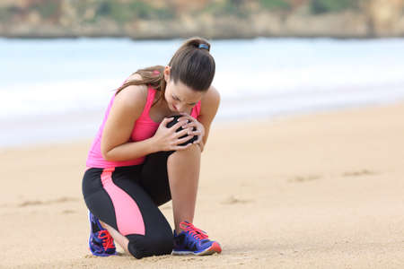Sportswoman complaining alone suffering knee ache after running outdoors on the beachの写真素材