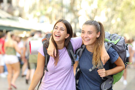 Front view portrait of two happy backpackers laughing enjoying vacation in a city streetの写真素材