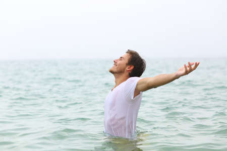 Side view portrait of a happy man stretching ams bathing on the beach