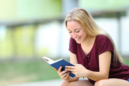 Happy student studying reading a paper book sitting outdoors in a campusの写真素材