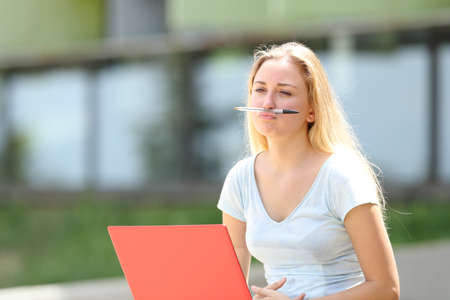 Bored student distracted playing with a pen outdoors in a campusの写真素材