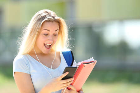 Surprised student walking checking smart phone messages outdoors in an university campusの写真素材