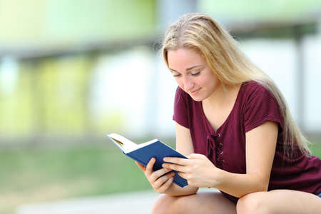 Relaxed student studying reading a paper book sitting outdoors in a campusの写真素材