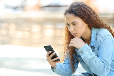 Serious mixed race woman using smart phone sitting in a parkの写真素材