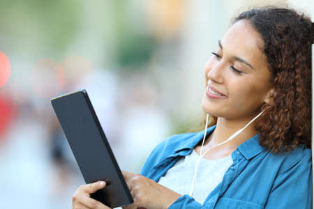 Happy mixed race woman listening music or watching media content with a tablet in the streetの写真素材