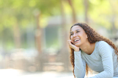 Happy mixed race woman dreaming looking at side sitting in a park with copy spaceの写真素材