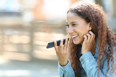 Happy mixed-race woman using voice recognition on smart phone to record messages in a parkの写真素材