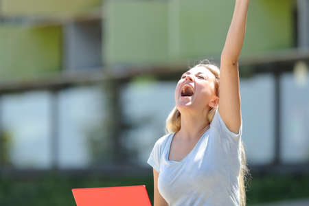 Excited student with laptop celebrating success raising arm outdoors in an university campusの写真素材