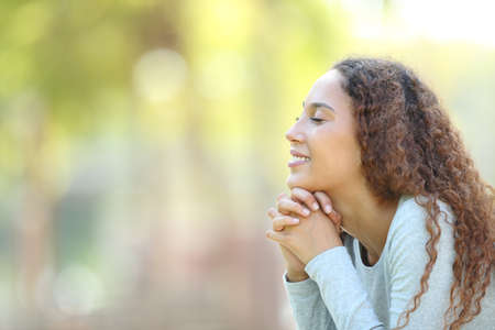 Side view portrait of a happy mixed race woman meditating and breathing fresh air outdoors in a park