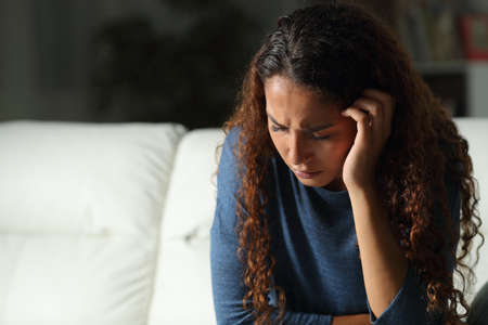 Sad mixed race woman complaining sitting on a couch in the living room at homeの写真素材