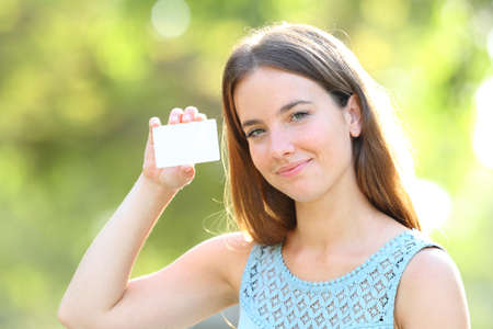 Woman holding and showing a blank credit card standing in a parkの写真素材