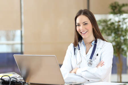 Happy female doctor posing looking at camera sitting at consultationの写真素材