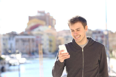 Happy man uses a smart phone walking on vacation in a coast townの写真素材