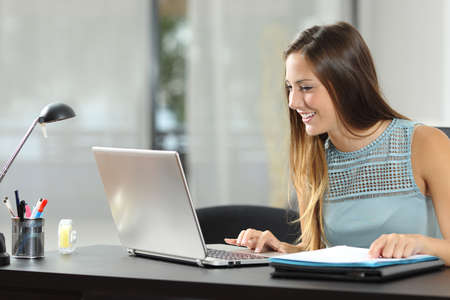 Happy entrepreneur working on line with a laptop and documents on a desk at homeの写真素材