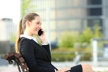 Happy businesswoman talking on smart phone sitting on a bench in a parkの写真素材