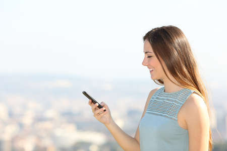 Profile of a woman using smartphone in the city outskirts in a sunny dayの写真素材