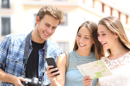Three happy tourists traveling checking smart phone gps and map in the street on summer vacationの写真素材