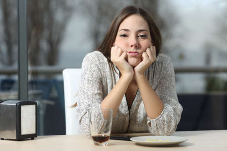Front view portrait of a bored woman in a bar looking at you a sad winter dayの写真素材