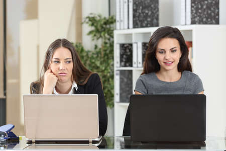 Front view of an envious employee looking her colleague working besideの写真素材