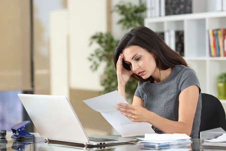Worried office worker complaining reading bad news in a paper letterの写真素材