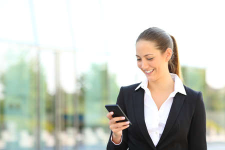 Happy businesswoman checking smart phone message walking in the streetの写真素材