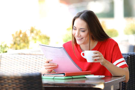 Happy student in red studying reading notes siting in a coffee shopの写真素材