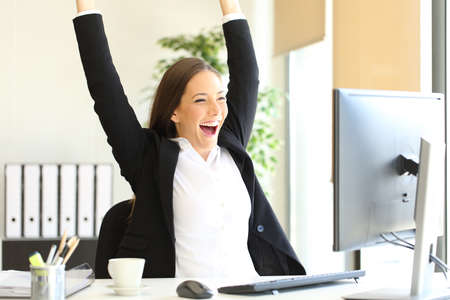 Excited businesswoman checking good news on computer celebrating success at officeの写真素材