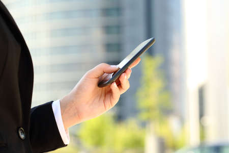 Close up of a businesswoman hand using a smart phone in the street with an office building in the backgroundの写真素材